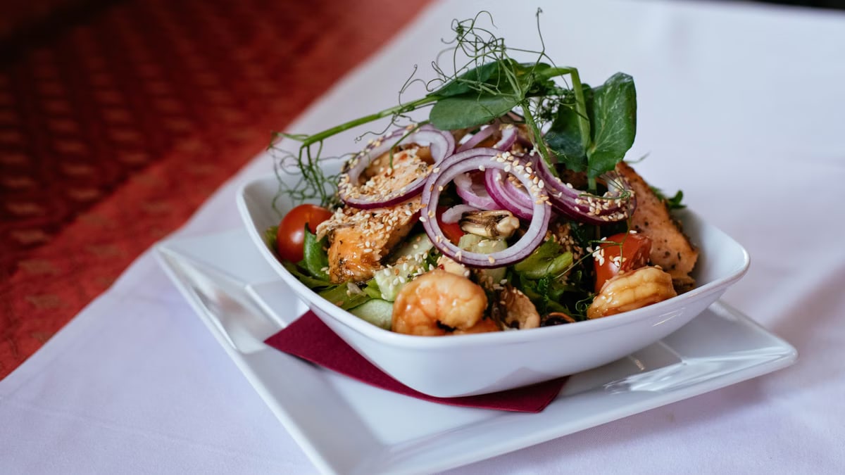 A delicious seafood salad featuring shrimp and salmon, topped with fresh greens and red onions.